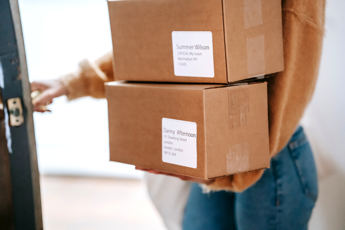 Crop unrecognizable woman carrying boxes and entering post office